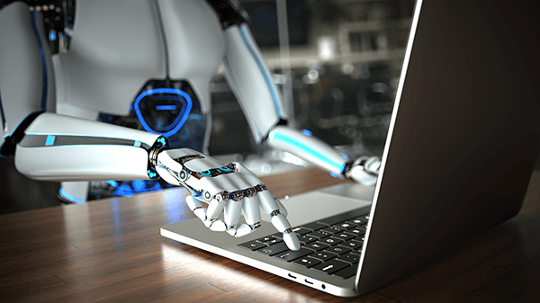 Humanoid robot sitting at a desk and typing on laptop.