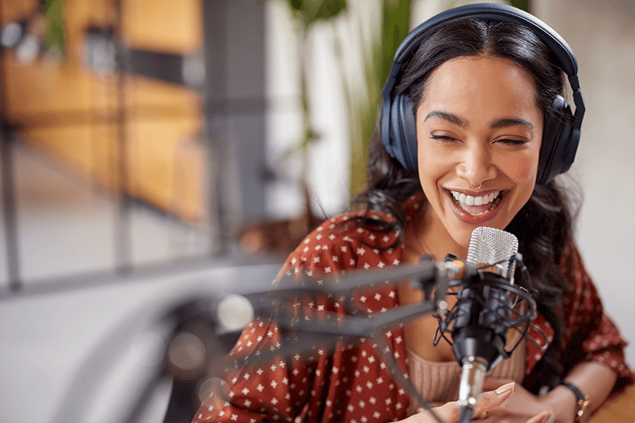 A woman in an orange blouse recording a podcast while wearing headphones.