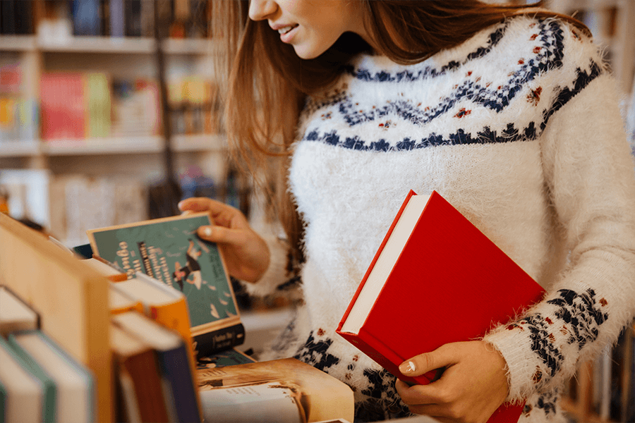 Young woman with long brown hair wearing a white sweater choosing books in library